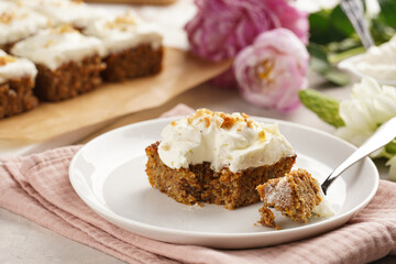 Homemade pastry carrot-walnut cake with grounded almonds and hazelnuts and white cream cheese top layer on white plate on pink napkin
