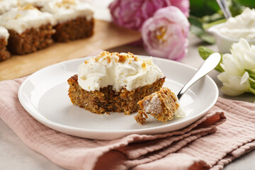 Homemade pastry carrot-walnut cake with grounded almonds and hazelnuts and white cream cheese top layer on white plate on pink napkin
