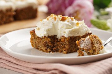 Homemade pastry carrot-walnut cake with grounded almonds and hazelnuts and white cream cheese top layer on white plate on pink napkin
