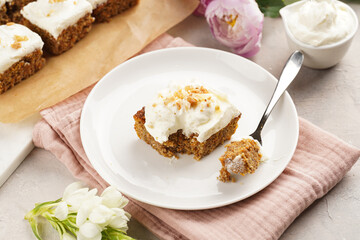 Homemade pastry carrot-walnut cake with grounded almonds and hazelnuts and white cream cheese top layer on white plate on pink napkin