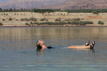 Young blonde woman relax, swim and float in the water of the Dead Sea in Jordan