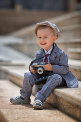 Portrait of a little kid boy photographer taking picture with retro vintage photo camera on the steps outside. Children's photo shoot. People childhood lifestyle concept.