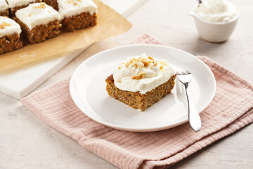 Homemade pastry carrot-walnut cake with grounded almonds and hazelnuts and white cream cheese top layer on white plate