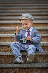 Portrait of a little kid boy photographer taking picture with retro vintage photo camera on the steps outside. Children's photo shoot. People childhood lifestyle concept.