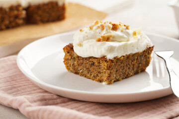 Homemade pastry carrot-walnut cake with grounded almonds and hazelnuts and white cream cheese top layer on white plate on pink napkin