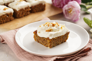 Homemade pastry carrot-walnut cake with grounded almonds and hazelnuts and white cream cheese top layer on white plate on pink napkin