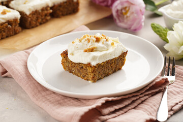 Homemade pastry carrot-walnut cake with grounded almonds and hazelnuts and white cream cheese top layer on white plate on pink napkin