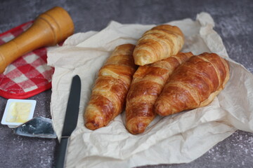 A pile of delicious fresh croissants served with butter on a gray table.