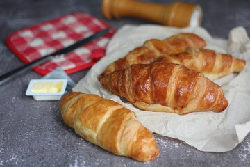 A pile of delicious fresh croissants served with butter on a gray table.