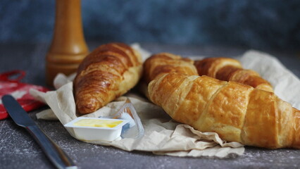 A pile of delicious fresh croissants served with butter. On a gray table with a blue background.