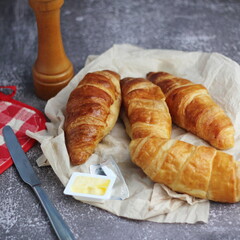 A pile of delicious fresh croissants served with butter on a gray table.