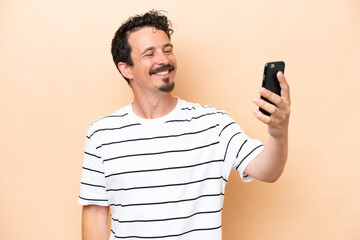 Young caucasian man isolated on beige background making a selfie