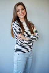 Smiling woman with long hair standing with crossed arms. Girl wearing jeans pants and striped shirt.