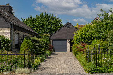 Car garage with a gray gate in a private home against a backdrop of greenery.