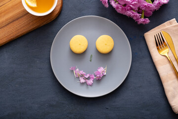 Smile with macaroons and petals on a plate on a dark stone table with flowers. Beautiful delicious dessert