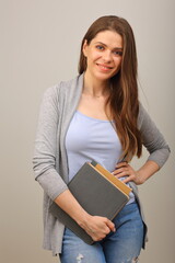 Smiling student with long hair dressed casual holding book,  isolated portrait on gray.