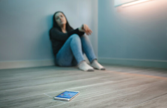 Unrecognizable desparate woman with phone addiction looking at her mobile sitting on the floor