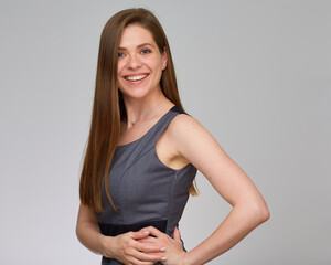 Smiling woman in gray dress keeps her hands on hip. Isolated studio portrait on gray.