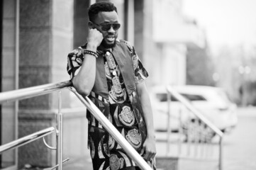 African stylish and handsome man in traditional outfit and sunglasses standing outdoor.