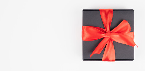 Black gift box with red silk ribbon isolated on white. Festive banner with copy space
