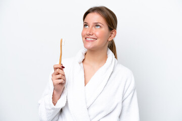 Young caucasian woman brushing teeth isolated on white background looking up while smiling