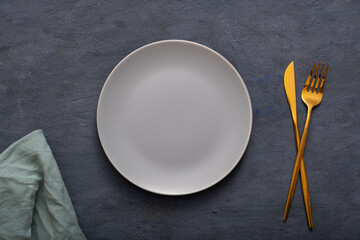Grey empty plate, cutlery and napkin on dark stone table. Top view, Table setting. background for...