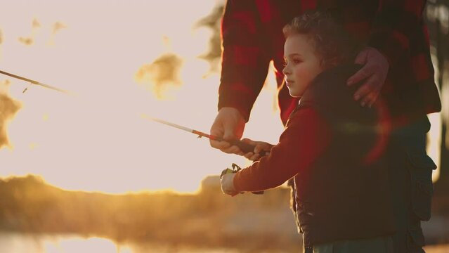 cute little boy is fishing, father or grandpa is helping child, active rest in nature, catch fish in lake
