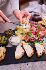 Woman spreading butter on grilled piece of baguette with Italian antipasto meat platter on background