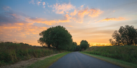 Fototapeta premium country road among meadows colorful sunset on background