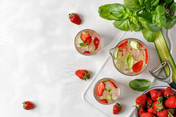 Ice cold summer drink. Glasses and jug of cold lemonade with strawberry, cucumber and basil. Tonic with berry and ice on marble board and white background. Copy space