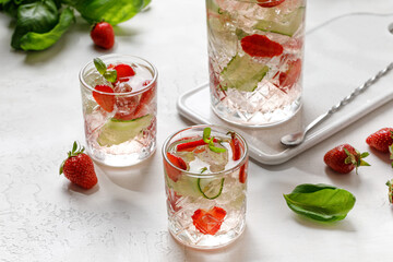 Cold lemonade with ice, strawberry, cucumber and basil on white background, fresh summer tonic in glass and jug. Cold drink.