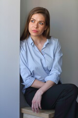 Young woman wearing blue shirt sit on stool near grey wall.