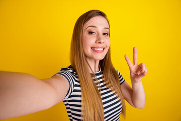 Profile side photo of young excited girl make selfie record video show peace v-symbol isolated over yellow color background