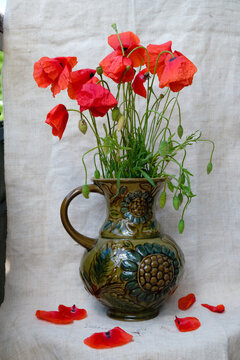 Poppy bouquet in a ceramic jug on a hemp canvas background. Still life in the Ukrainian folk style. Vertical image.