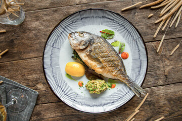 Top view on plate of grilled gourmet fish on wooden background