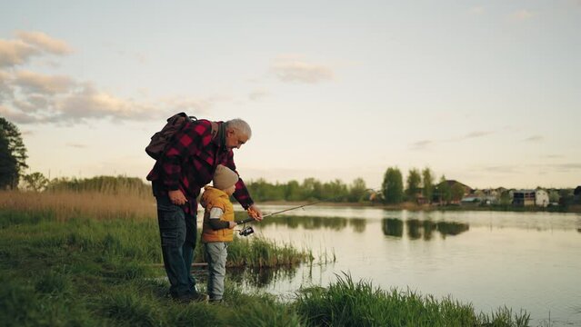 old man and his grandson are fishing on coast of beautiful pond, little boy and his grandfather