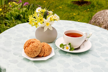 A cup with tea and dessert on a plate in the fresh air of a garden plot. A decorative bouquet of flowers in a vase on the table.