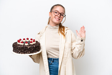 Young caucasian woman holding a Birthday cake isolated on white background saluting with hand with happy expression