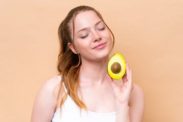 Young caucasian girl isolated on beige background holding an avocado. Close up portrait