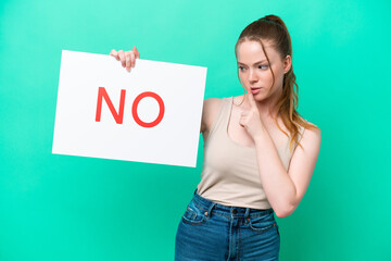 Young caucasian woman isolated on green background holding a placard with text NO doing silence gesture