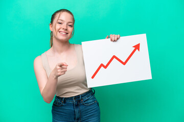 Young caucasian woman isolated on green background holding a sign with a growing statistics arrow symbol and pointing to the front