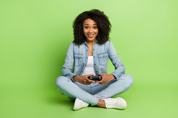 Full size photo of young cheerful lady sit floor play game console weekend isolated over green color background