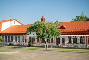 Fototapeta na wymiar One-storey building with red-tiled roof and green tree in front of entrance