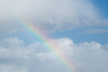 Colourful rainbow against bright clouds and blue sky, abstract background