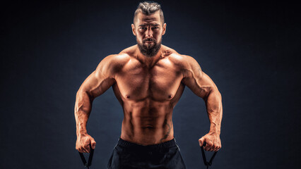 Fototapeta na wymiar Muscular guy stretching rubber resistance bands in dark background
