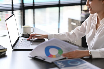 Asian woman worker using laptop computer and checking reports at office desk