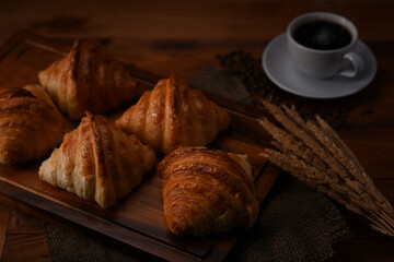 Fresh homemade butter croissant in tray decorated with wheat on wooden table. Levitation, bread bakery products cafe concept