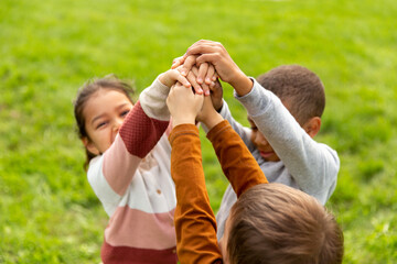childhood, leisure and people concept - group of children stacking hands at park