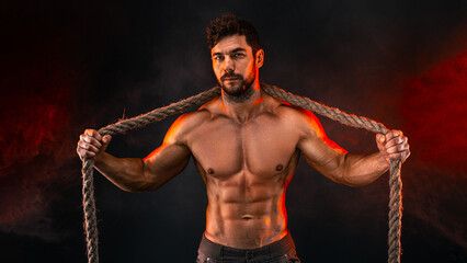 Shirtless athletic man posing with rope on neck, shoulders in front of brick wall. Strength and motivation