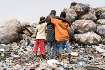 Three young African children standing hopelessy in front of a garbage mountain, symbolizing health...